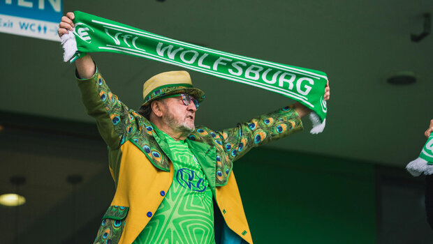 Ein Fan vom VfL Wolfsburg hält einen Schal in die Luft.