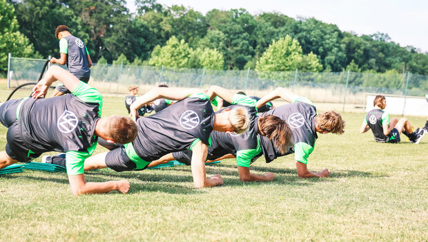 Die Spieler der VfL Wolfsburg-Akademie machen auf dem Rasen eine seitliche Plank.