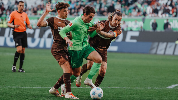 VfL-Wolfsburg-Spieler Jakub Kaminski wird von zwei Gegenspielern gefoult.