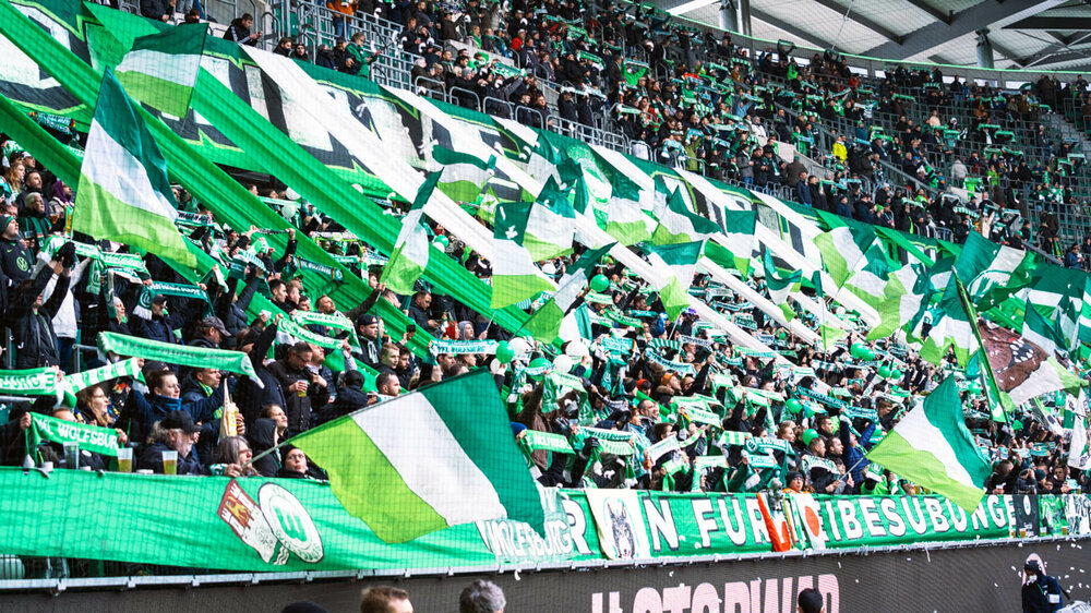 Die Fans des VfL Wolfsburg schwenken in der Fankurve ihre grün-weißen Fahnen,