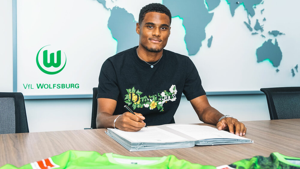 VfL Wolfsburg Spieler Sarr schaut in die Kamera, vor ihm liegt sein Vertrag, den er unterzeichnet.