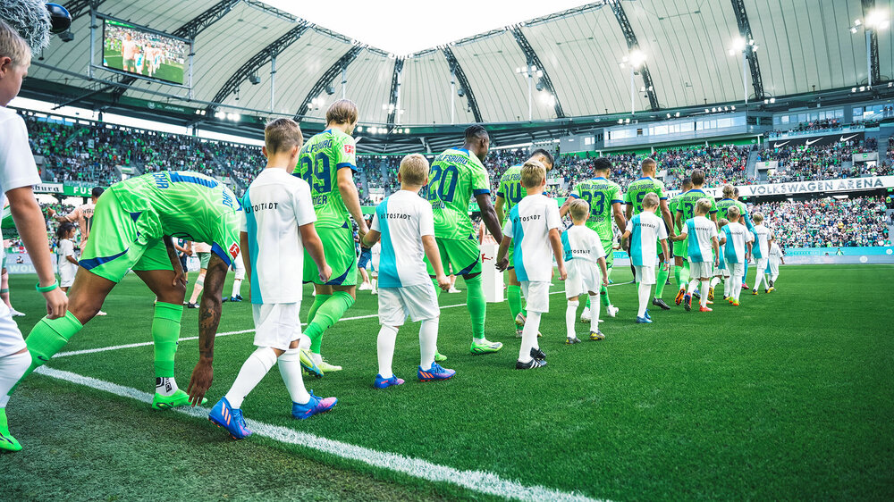 Die Spieler des VfL Wolfsburg laufen mit Kindern in die Volkswagen Arena ein.