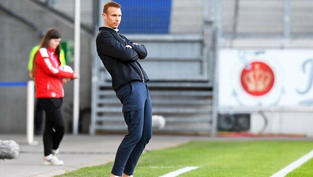 VfL Wolfsburg Trainer Tommy Stroot am Spielfeldrand mit zurückgelehnten Oberkörper.