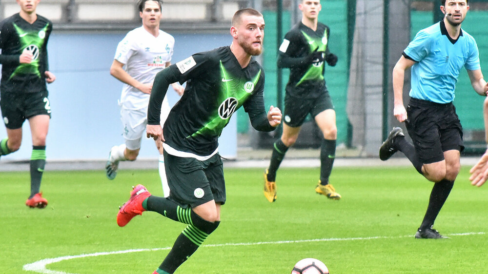 Ole Pohlmann von der U19 des VfL Wolfsburg dribbelt im Regen mit Ball durch das Mittelfeld.