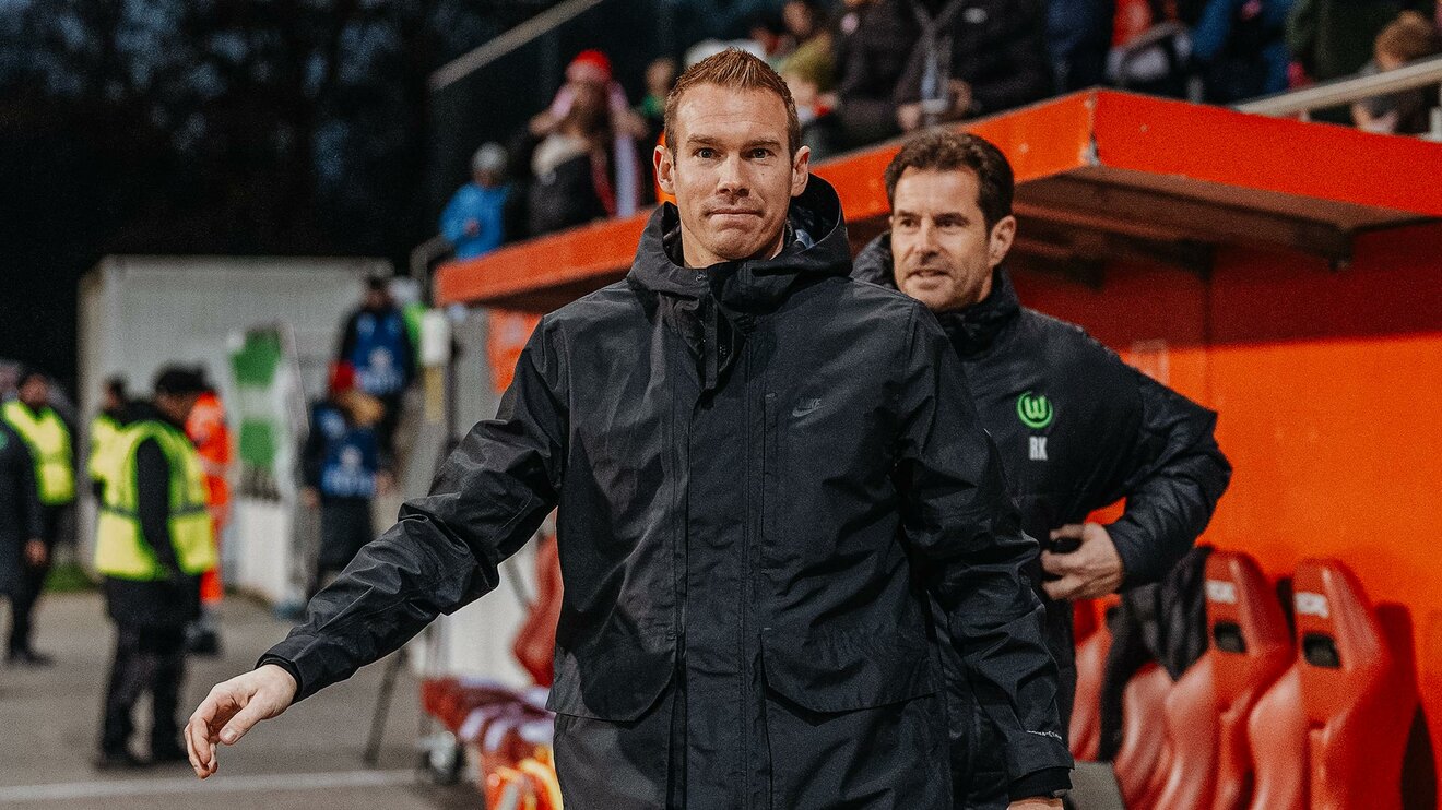 VfL-Wolfsburg-Trainer Tommy Stroot steht vor der Trainerbank.