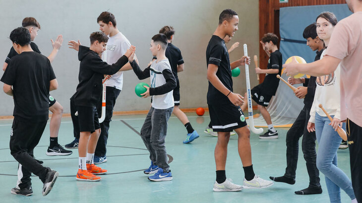 Kinder spielen zusammen mit U14-Spieler vom VfL-Wolfsburg im Landesbildungszentrum für Hörgeschädigte. Sie klatschen sich ab.
