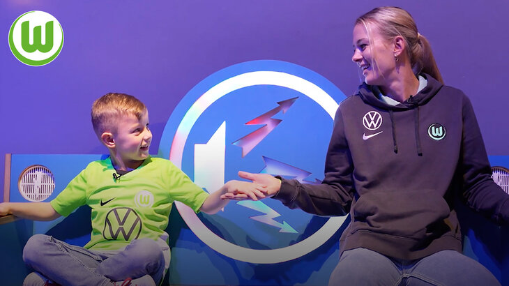 Merle Frohms hält die Hand eines kleinen Jungen in VfL-Wolfsburg-Trikot.