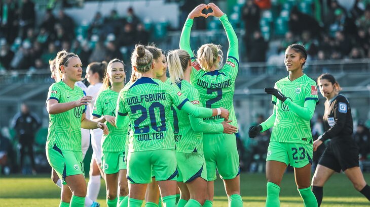 Die Frauen des VfL-Wolfsburg freuen sich gemeinsam auf dem Platz über ein gewonnenes Spiel. Eine Spielerin zeigt eine Herzgeste zu den Fans.