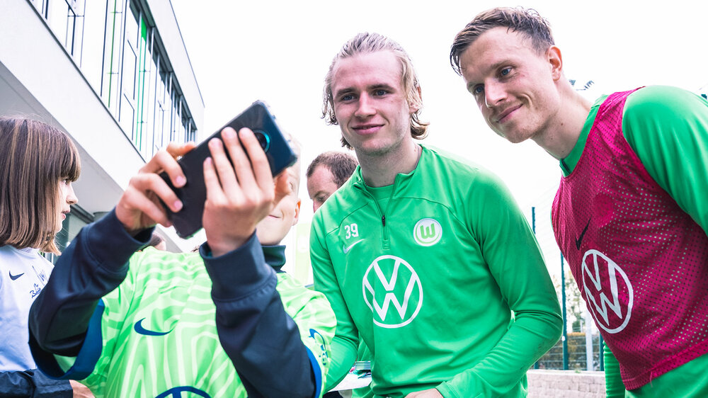 Die beiden VfL-Wolfsburg-Spieler Patrick Wimmer und Yannick Gerhardt posieren für ein Selfie mit einem jungen Fan.