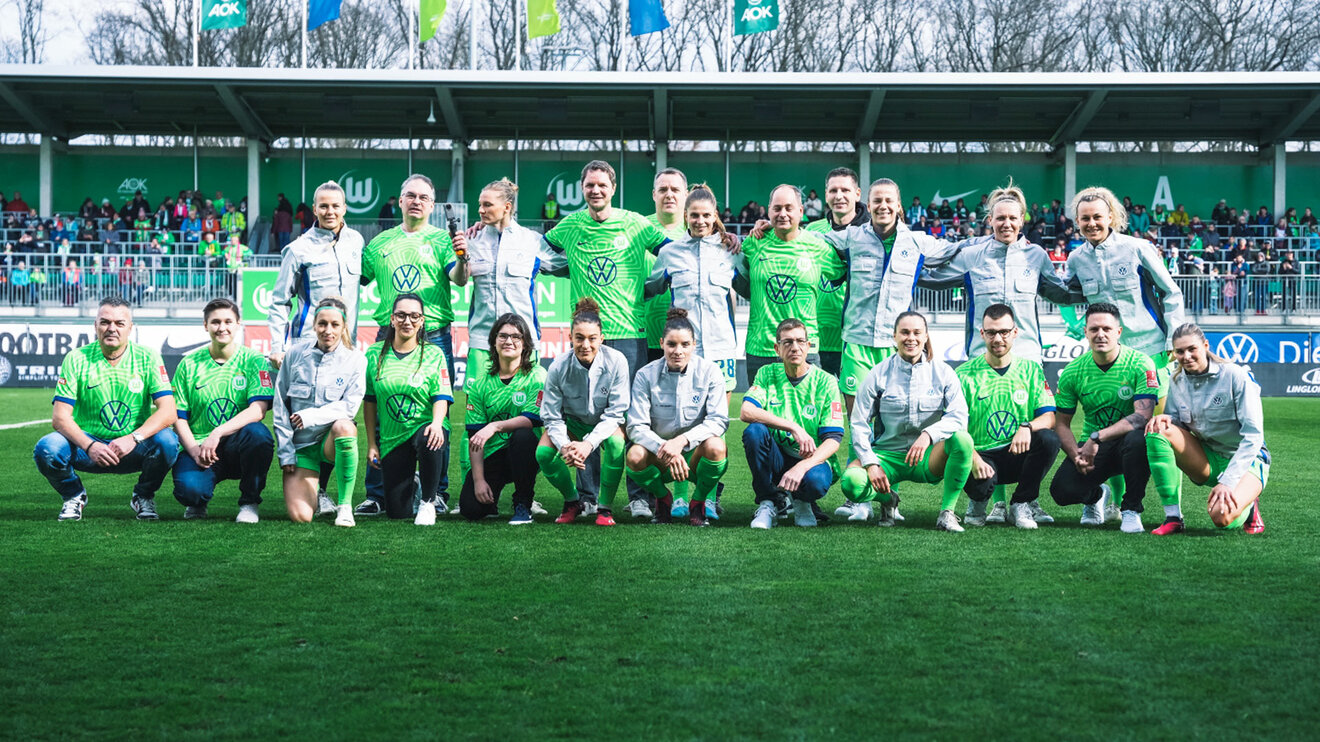 Ein Bild der VfL-Wolfsburg-Spielerinnen in der Volkswagen-Arbeitsjacken mit Mitarbeitern von VW.