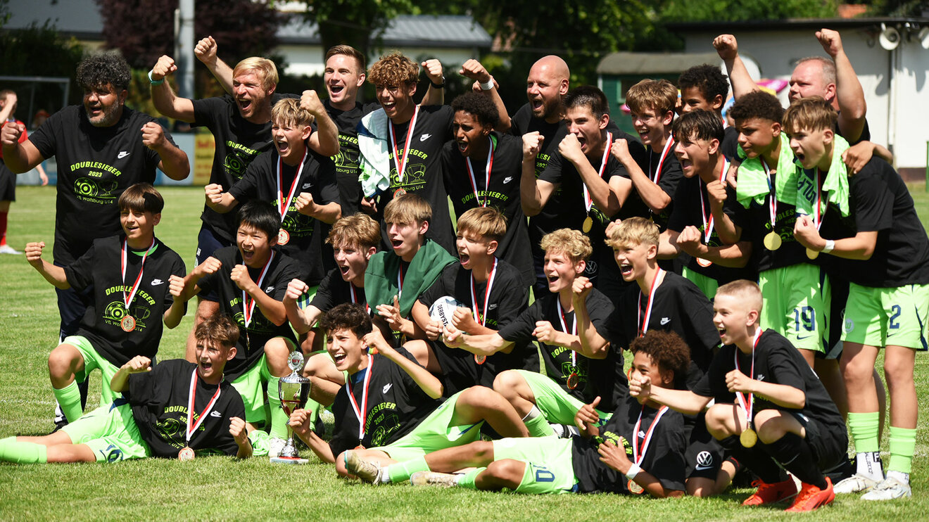 Die U14 Mannschaft des VfL Wolfsburg posiert für ein Mannschaftsfoto mit Pokal und jubelt.