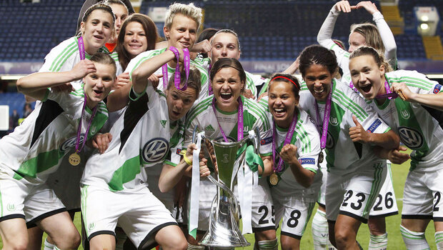 Die ehemalige Frauenmannschaft des VfL Wolfsburg jubelt auf einer Siegerehrung mit einem Pokal und Medaillen.