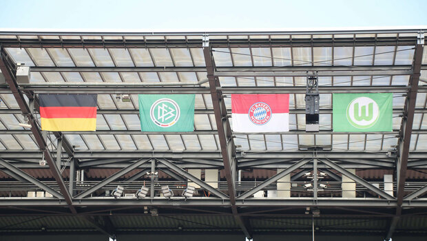 Die Flaggen von Deutschland, dem Pokal, Bayern und vom VfL Wolfsburg hängen am Stadiondach.