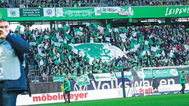 Die Fans der Frauen des VfL Wolfsburg wedeln mit grün-weißen Fahnen und stehen hinter dem Tor.