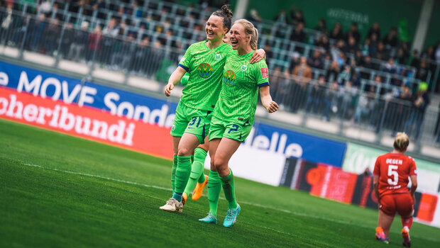 VfL Wolfsburg Spielerinnen Bremer und Hegering laufen lachend Arm in Arm über das Spielfeld.