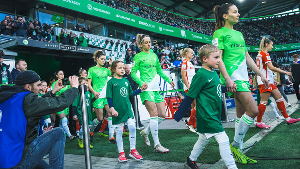 Die Frauen des VfL Wolfsburg laufen mit Einlaufkinder in die Volkswagen-Arena ein.