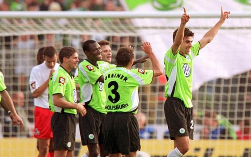 Die VfL Wolfsburg Spieler aus dem Jahr 1999 jubeln in Tornähe mit gehobenen Händen.