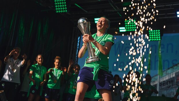 Katarzyna Kiedrzynek vom VfL Wolfsburg hebt auf der Bühne den Pokal in die Luft und jubelt mit ihrem Team.