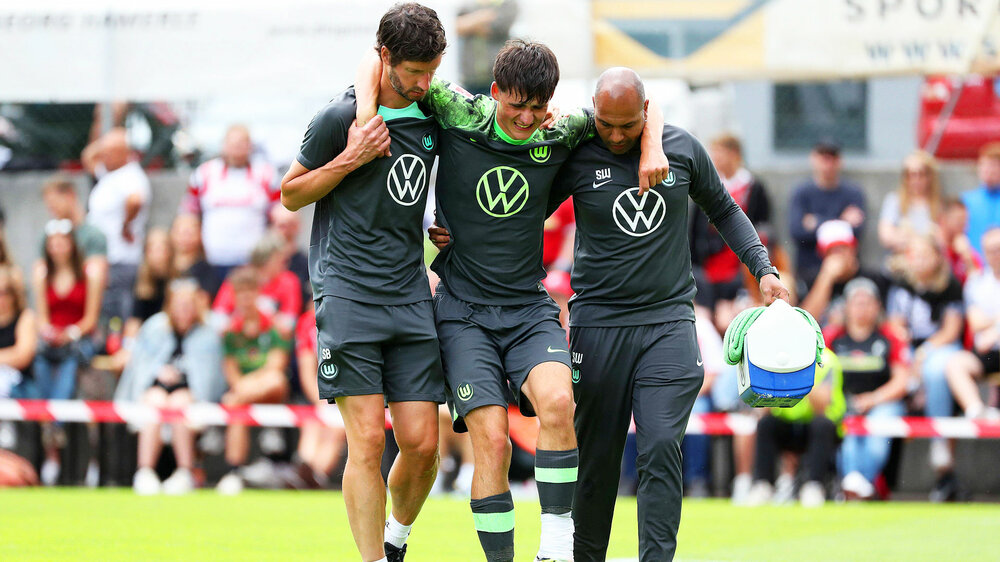 VfL-Wolfsburg-Spieler Lange geht nach einer Verletzung mit Unterstützung vom Feld.