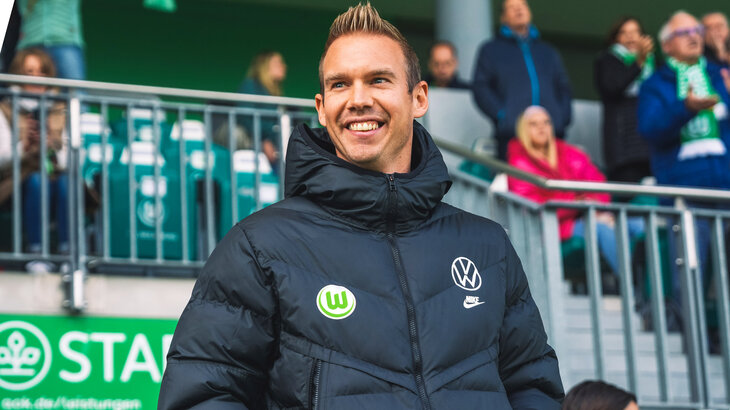 Der VfL-Wolfsburg-Trainer Tommy Stroot steht lächelnd im Stadion.