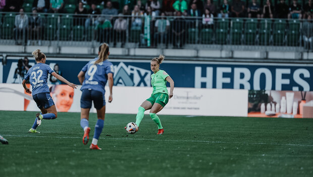 Janina Minge vom VfL Wolfsburg spielt mit dem rechten Fuß den Ball. Auf sie drauf zu kommen zwei Gegenspielerinnen.