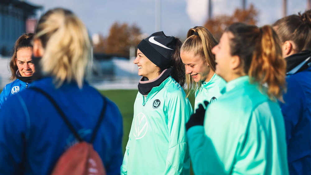 Die VfL-Wolfsburg-Spielerinnen stehen lachend zusammen auf dem Trainingsplatz..