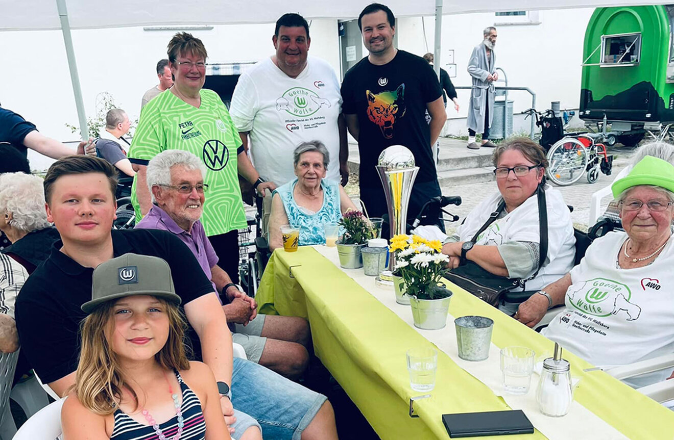 Mitglieder des VfL Wolfsburg Fanclubs "Goethewölfe" sitzen zusammen an einem Tisch und schauen in die Kamera.