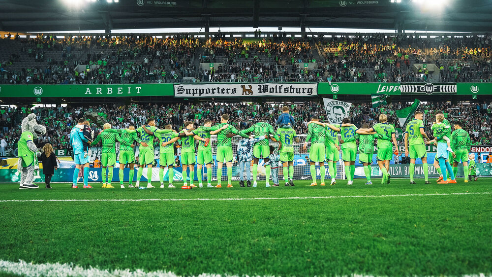 Die Männer des VfL Wolfsburg bilden eine lange Reihe und jubeln zu ihren Fans in der Kurve.