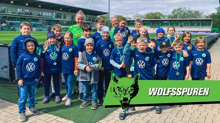 Die beiden VfL-Wolfsburg-Spielerinnen Pia-Sophie Wolter und Rebecka Blomqvist posieren mit vielen Kindern vor dem Spielfeld des AOK Stadions.