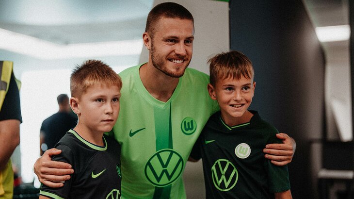 VfL-Wolfsburg-Spieler Mattias Svanberg steht Arm in Arm mit zwei kleinen Fans.