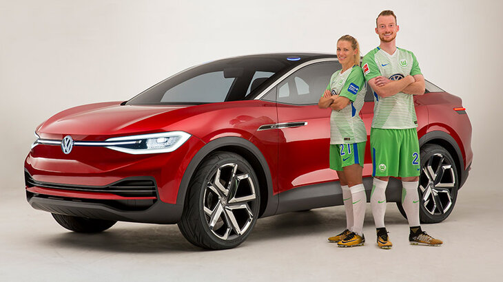 Lara Dickenmann und Maximilian Arnold posieren in VfL Wolfsburg-Trikots vor dem neuen Volkswagen.