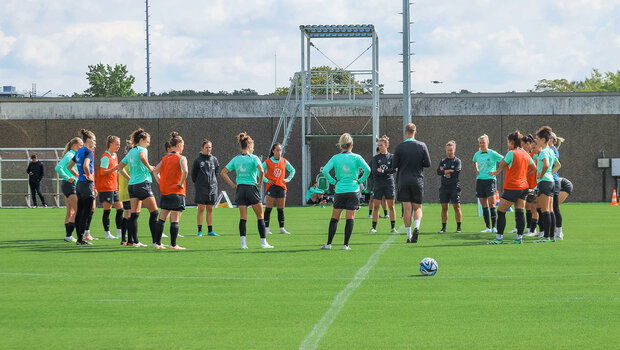 Die Spielerinnen des VfL Wolfsburg stehen auf dem Trainingsplatz am Mittelkreis und lauschen dem Trainerteam.