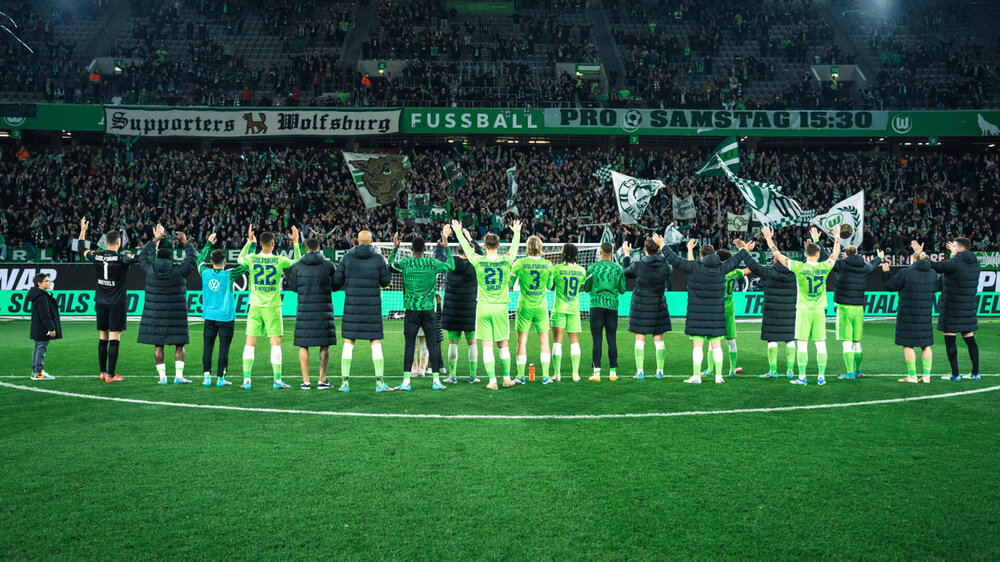 Die Männer des VfL Wolfsburg stellen sich in einer Reihe in Richtung der Fankurve auf und kommunizieren mit den Fans.