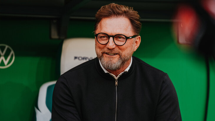 VfL-Trainer Ralph Hasenhüttl sitzt lächelnd auf der Trainerbank.