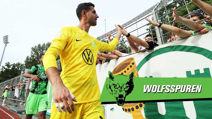 Koen Casteels klatscht bei den Wolfsburg Fans ein, davor befindet sich eine VfL Wolfsburg Grafik mit der Aufschrift "Wolfsspuren".