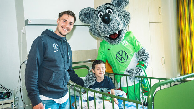 VfL-Wolfsburg-Spieler Kilian Fischer besucht gemeinsam mit Wölfi das Kinderkrankenhaus. Hier macht er ein Foto mit einem kleinen Kind.