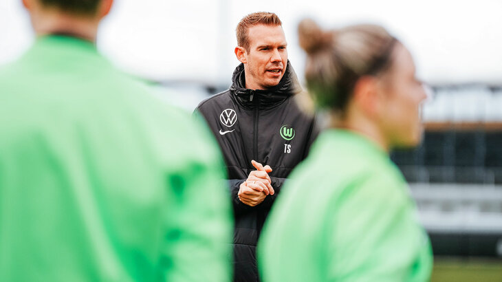VfL-Wolfsburg-Trainer Tommy Stroot steht auf dem Trainingsplatz vor den Spielerinnen.