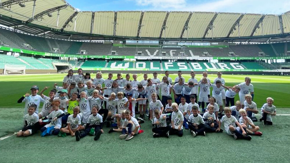 VfL Wolfsburg Fußballschule-Teilnehmer posieren für ein Gruppenfoto auf dem Rasen der Volkswagen Arena.