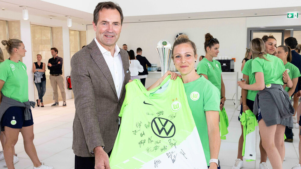 Svenja Huth vom VfL Wolfsburg hält zusammen mit VW Markenchef Thomas Schäfer ein signiertes Trikot in die Kamera.