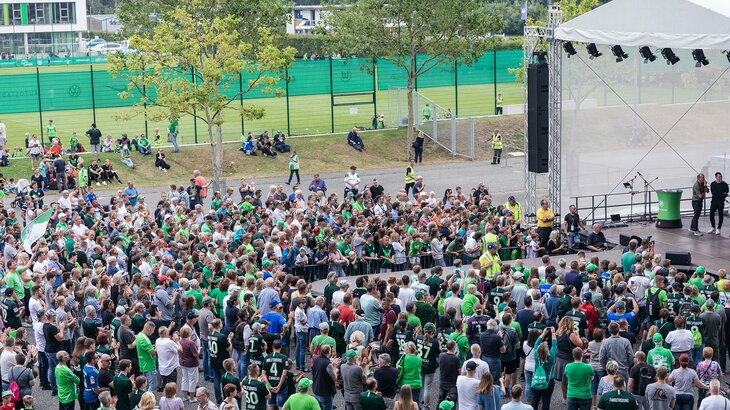 Fans des VfL Wolfsburg stehen vor einer Bühne.
