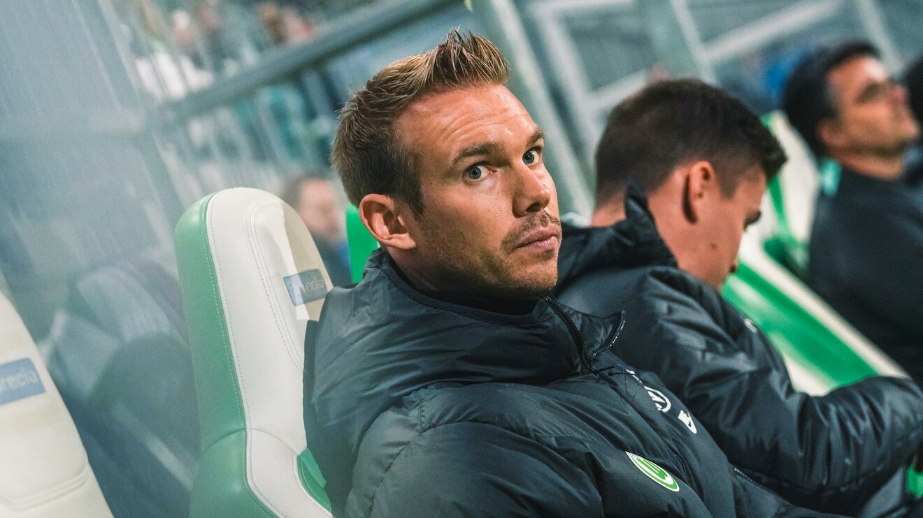 Tommy Stroot, Trainer der VfL Wolfsburg Frauen, sitzt auf der Trainerbank und schaut auf das Spielfeld.