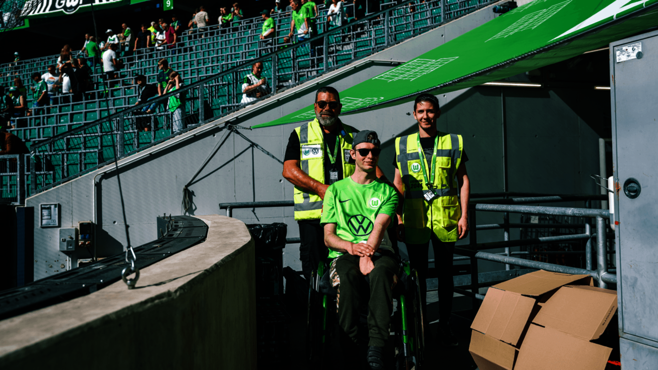 Aushilfen des VfL Wolfsburg mit einem Fan im Rollstuhl.