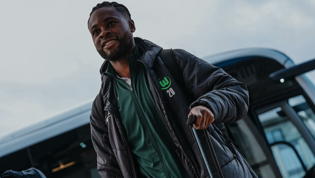Der VfL-Wolfsburg-Spieler Ridle Baku läuft mit seinem Koffer vor einem Bus.