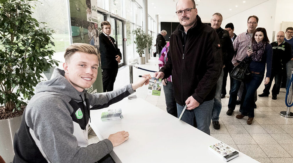 VfL Wolfsburg-Profi Yannick Gerhardt überreicht einem Fan ein Autogramm.