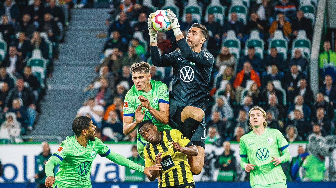 VfL-Wolfsburg-Torwart Koen Casteels springt mit mehreren Mit- und Gegenspielern in die Luft und fängt den Ball.