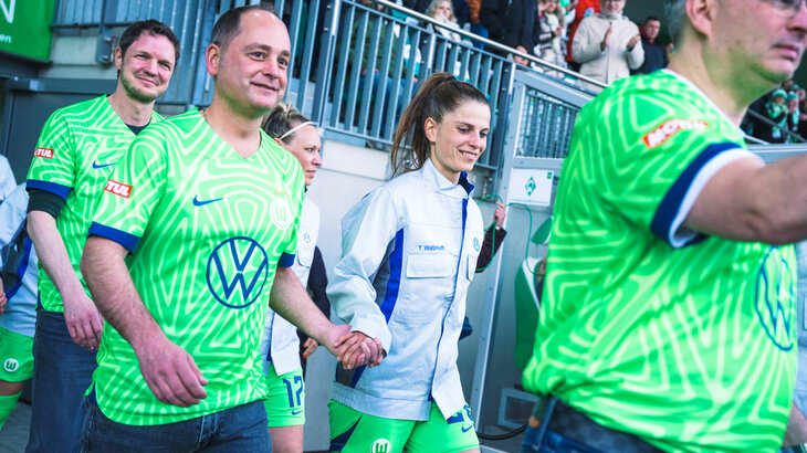 Die VfL-Wolfsburg-Spielerin Tabea Waßmuth läuft in der Volkswagen-Arbeitsjacken mit einem Mitarbeiter auf das Spielfeld.