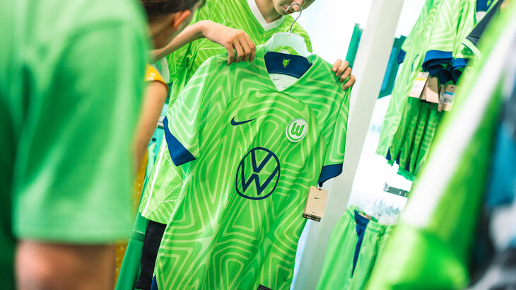 Ein grünes Heimtrikot des VfL Wolfsburg wird in Händen gehalten.