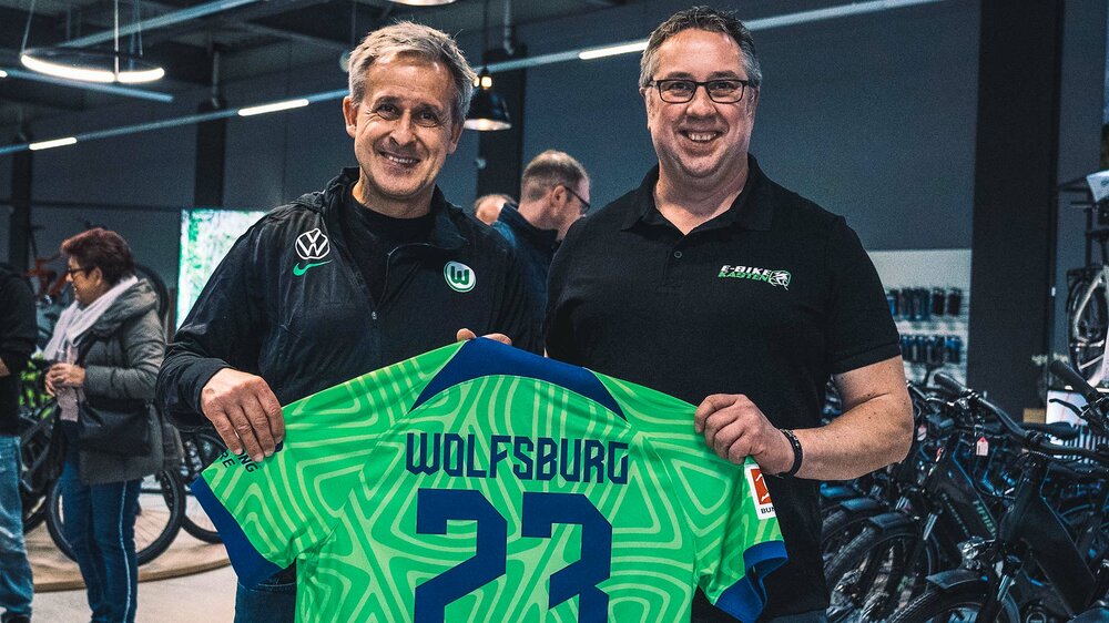VfL Wolfsburg Funktionär Pierre Littbarski posiert mit einem Mitarbeiter von E-Bike Kasten und einem Trikot.