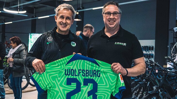 VfL Wolfsburg Funktionär Pierre Littbarski posiert mit einem Mitarbeiter von E-Bike Kasten und einem Trikot.