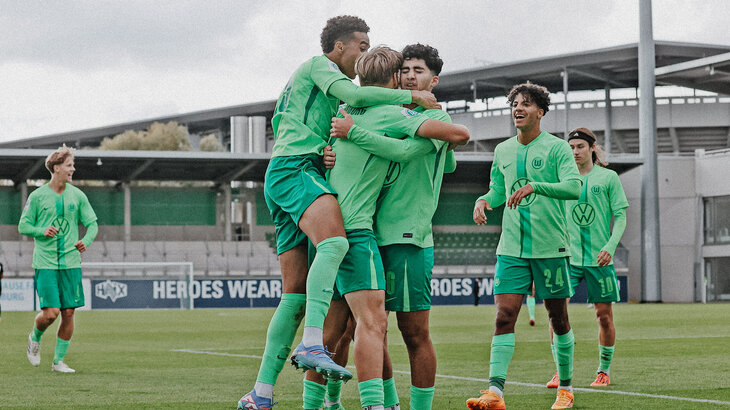 Spieler der U19-Mannschaft des VfL Wolfsburg stehen beisammen, umarmen sich und jubeln.